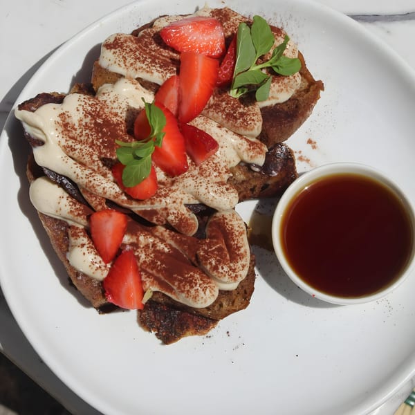 Vegan French toast with cream, cocoa powder, strawberries, and mint, served with syrup.