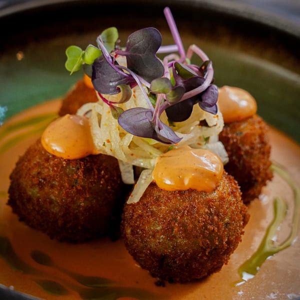 Close-up of crispy vegan arancini balls topped with orange sauce and microgreens on a green plate.