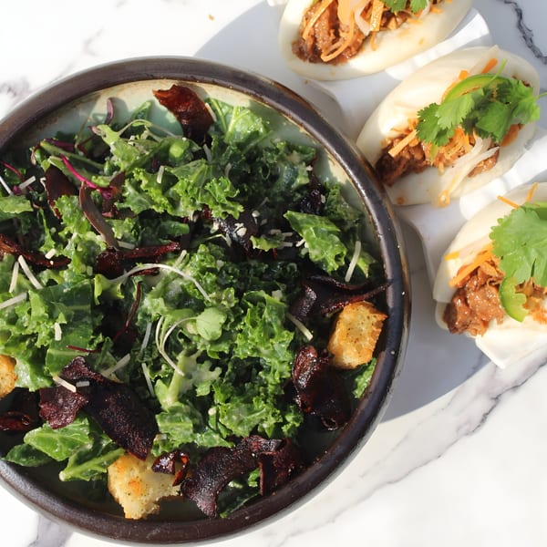 Vegan Caesar salad with croutons and three bao buns with filling and cilantro on marble.